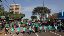 Crianças e adultos de mãos dadas participam de desfile em Dourados, com público nas laterais da avenida. Foto de arquivo.