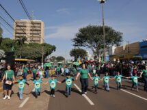 Crianças e adultos de mãos dadas participam de desfile em Dourados, com público nas laterais da avenida. Foto de arquivo.