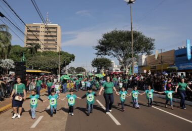 Crianças e adultos de mãos dadas participam de desfile em Dourados, com público nas laterais da avenida. Foto de arquivo.