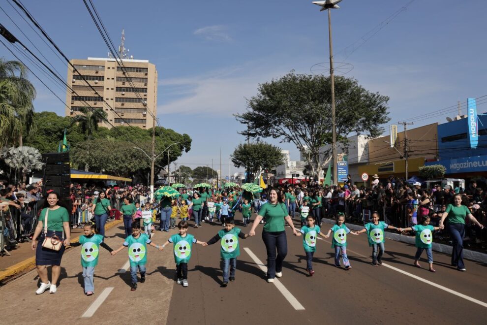 Crianças e adultos de mãos dadas participam de desfile em Dourados, com público nas laterais da avenida. Foto de arquivo.