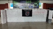 Pacotes de cigarros apreendidos expostos diante de painel da Força Tática do 14º BPM