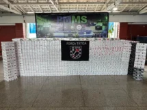 Pacotes de cigarros apreendidos expostos diante de painel da Força Tática do 14º BPM