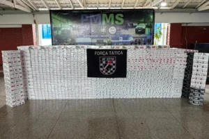 Pacotes de cigarros apreendidos expostos diante de painel da Força Tática do 14º BPM