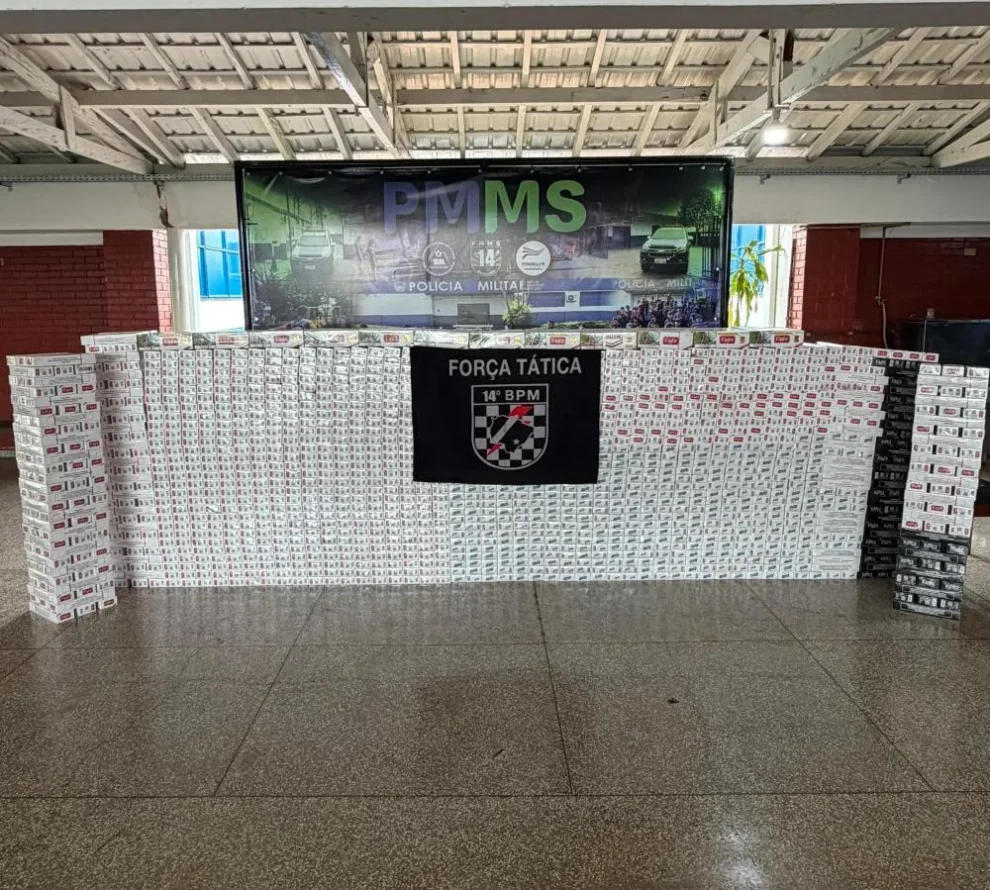 Pacotes de cigarros apreendidos expostos diante de painel da Força Tática do 14º BPM
